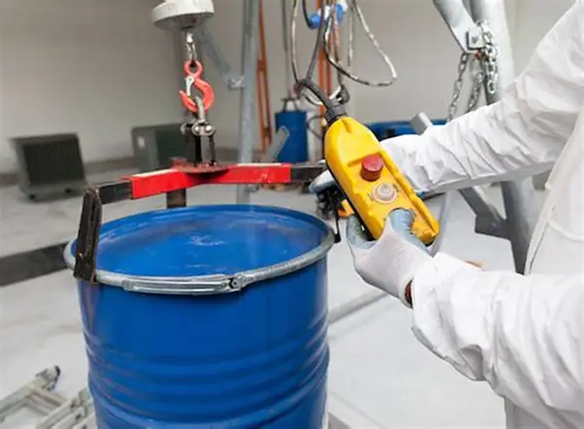 Operator in protective clothing lifting a reagent drum with a hoist and drum clamp