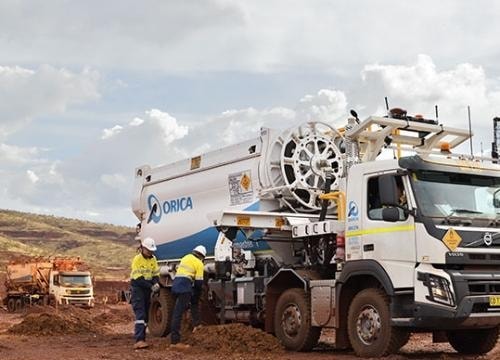 Crew in hi-vis and hard hats working at the rear of an Orica bulk explosives delivery truck on a red-earth mine bench